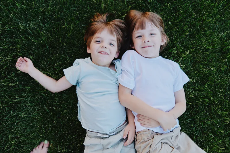 Happy children lying on green grass, enjoying a sunny day while playing outdoors, full of joy and laughter in a vibrant setting.