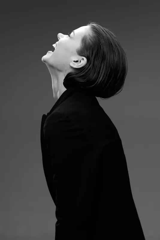 Black and white laughing woman in dark clothing with short hair expressing joy and freedom in studio setting.