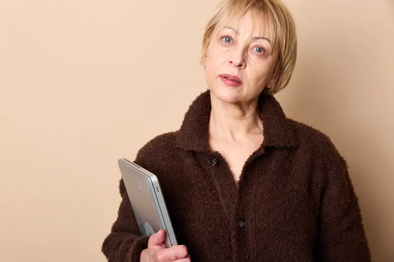 Woman portrait tablet senior technology indoors beige communication digital device, mature blond hair, holding tablet, calm thoughtful expression, soft studio light, concept learning, wellness