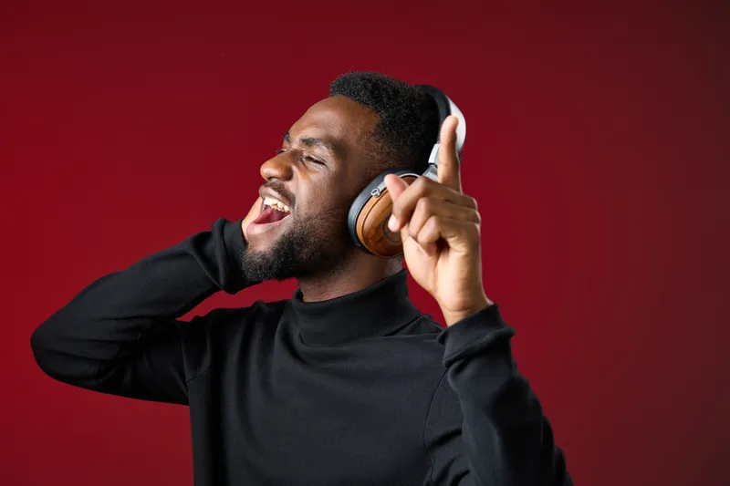 A joyful young Black man singing and enjoying music with headphones on a vibrant red background, conveying happiness and passion for music