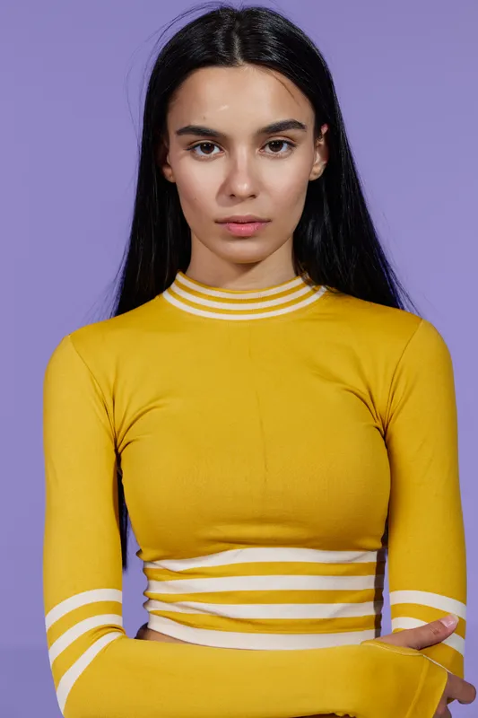 Sport fitness woman wearing yellow athletic top poses confidently against purple background, showcasing focus, strength, and determination in studio shot.