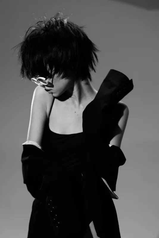 Black and white portrait of a young woman with short hair wearing glasses and dark clothing, captured in a stylish and moody atmosphere.