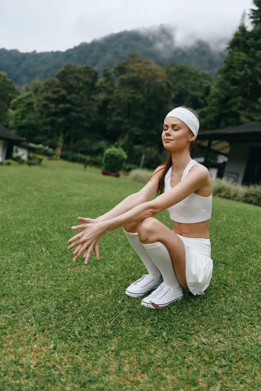 Young athletic woman performing a squat exercise outdoors in a serene green landscape, showcasing fitness, health, and determination in a seasonal setting