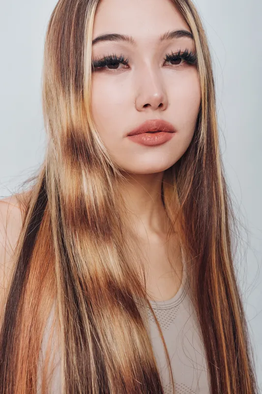 Young woman with long straight hair and natural makeup posing against white background for beauty portrait, skincare, haircare, and fashion concept in studio lighting