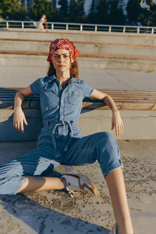 lifestyle woman in modern boho-western denim street style sitting relaxed outdoors with film color tones and casual attitude in warm sunlight