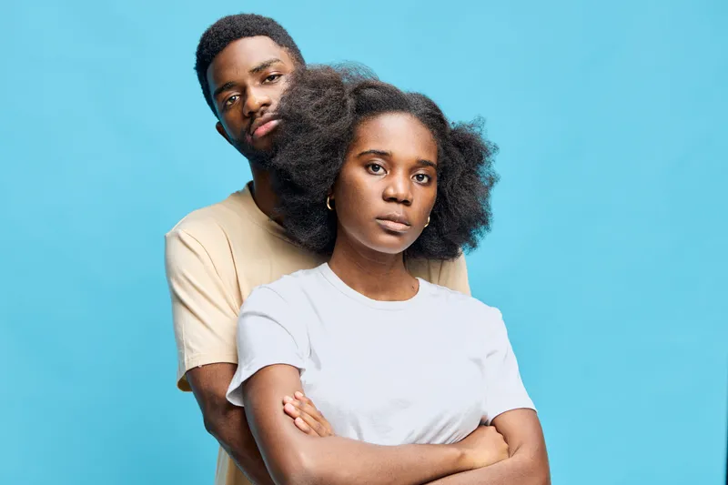 African couple expressing confidence and unity in casual outfits against a vibrant blue background, showcasing modern lifestyle and togetherness