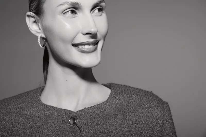 Smiling young Caucasian woman with light skin and short hair looks aside in studio. Concept of happiness, beauty, and confident female model in black and white portrait photography.