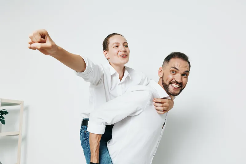 A professional businessman is shown with a smile, lifting a colleague in a playful pose against an isolated colored background, expressing energy, confidence, and upbeat teamwork.