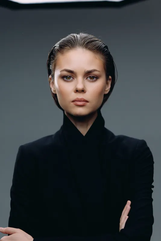Serious woman with wet hair wearing black turtleneck, posing against dark background with calm expression and confident posture