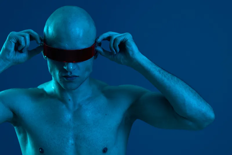 Bold man adjusting futuristic eyewear, showcasing a striking blue hue with a sleek modern aesthetic. Captivating elements evoke a sense of innovation and style.