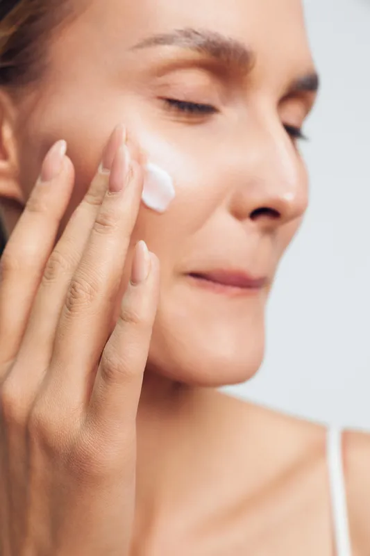 Woman close up on face, skincare, beauty cream applying with cotton, moisturizing spa routine, calm expression, smooth glowing skin, hands on cheek and eye, natural light