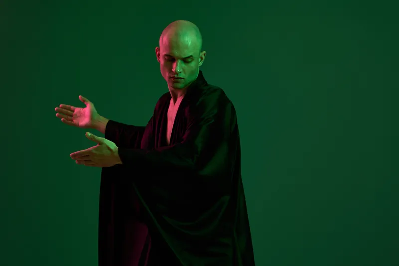 Elegant man in black attire gestures expressively against a vibrant green backdrop, capturing a sense of creativity and passion. Perfect for artistic themes or performances.