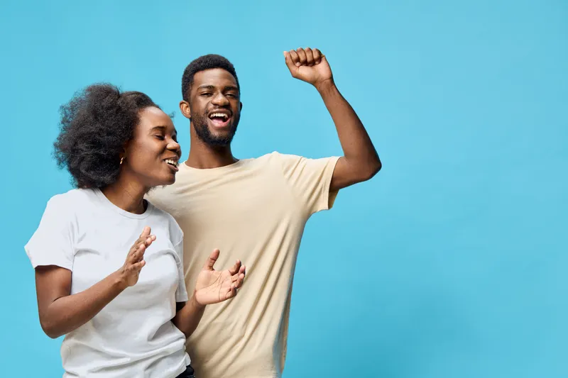 Joyful African American couple celebrating with laughter and happy expressions against a bright blue background, perfect for cheerful moments and relationships