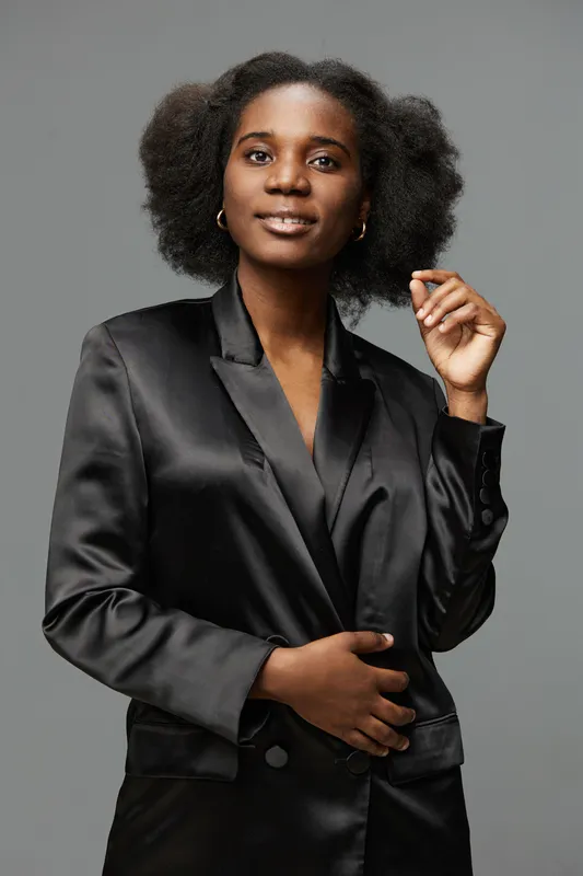 Elegant woman in a black satin blazer showcasing natural beauty and confidence against a neutral background, ideal for fashion and empowerment themes