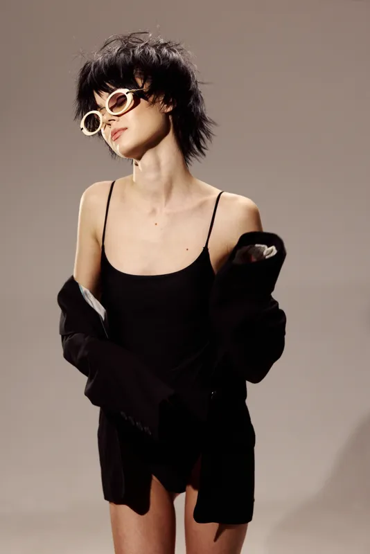 Stylish woman wearing black dress and sunglasses posing with confidence in neutral background fashion concept