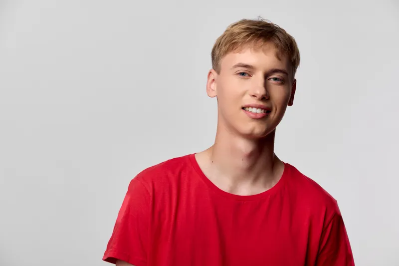 Smiling man wearing a bright red shirt stands against a minimalist studio backdrop, casual fashion vibe, relaxed confidence and approachable energy for lifestyle imagery