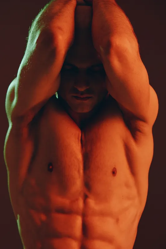 A focused man showcasing strength and determination in a dramatic light setting. His muscular physique emphasizes the intensity of the moment and the energy around him.