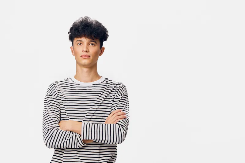 portrait of young man in striped shirt with crossed arms against white background, standing confidently with neutral facial expression, casual style