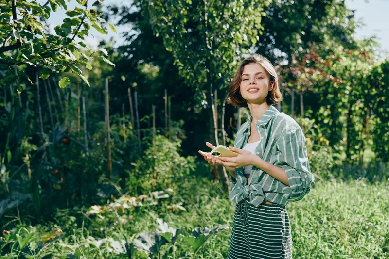 A young woman stands in a sunlit garden, smiling, holding fresh fruit in her hands.