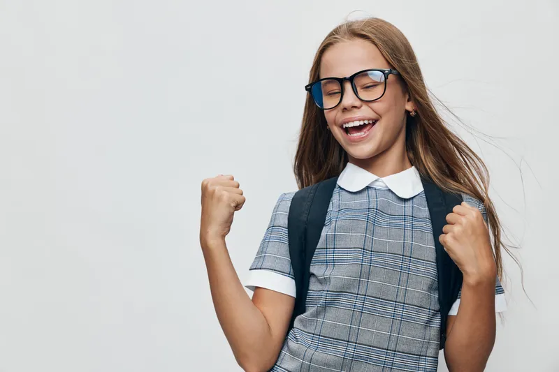 Girl with backpack and glasses smiling happily and celebrating success or achievement on white background. Child student with school bag showing excitement and confidence in education.