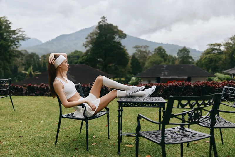 Young Asian woman in sporty outfit sitting on a garden chair with mountains in the background, exuding confidence and joy in nature s beauty
