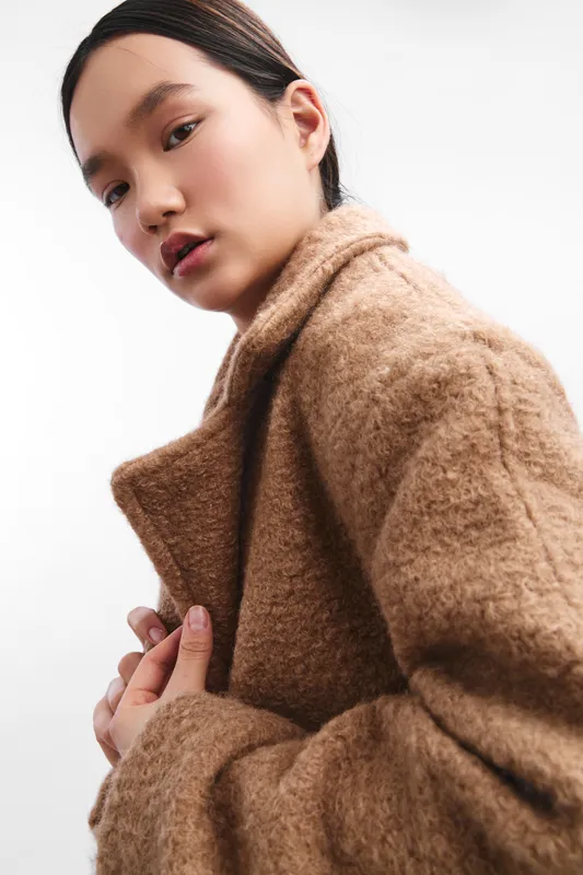 asian woman wearing a plush coat poses in a clean studio setting, close portrait with soft lighting, conveying warmth, style, and confident presence.
