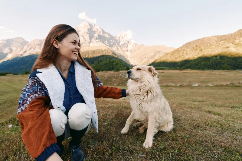 Woman dog mountains meadow smiling pet outdoors nature sitting happy in a mountain meadow, she is petting her dog and smiling during a relaxed outdoor moment with warm sunlight.