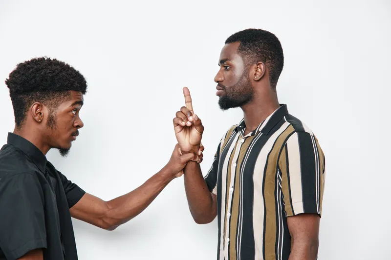 Two african american men with dark skin having serious conversation and disagreement with hand gesture on white background. Young black males in casual clothes facing each other.