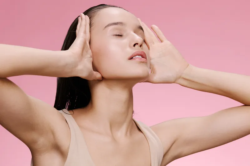 Serene young model with a natural glow, showcasing emotional tranquility against a soft pink background, embodying beauty and self care concepts