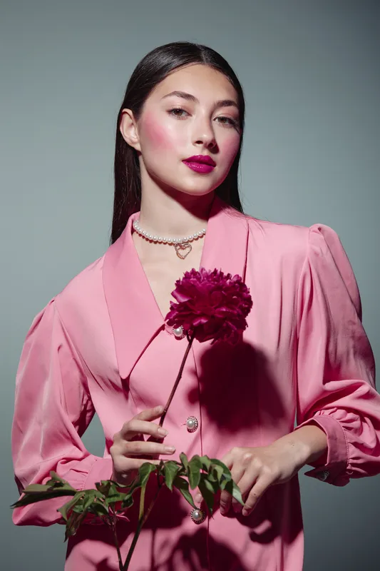 Elegant woman wearing vintage pink dress posing with fuchsia flower, makeup and accessories in stylish beauty fashion photo autumn lighting.