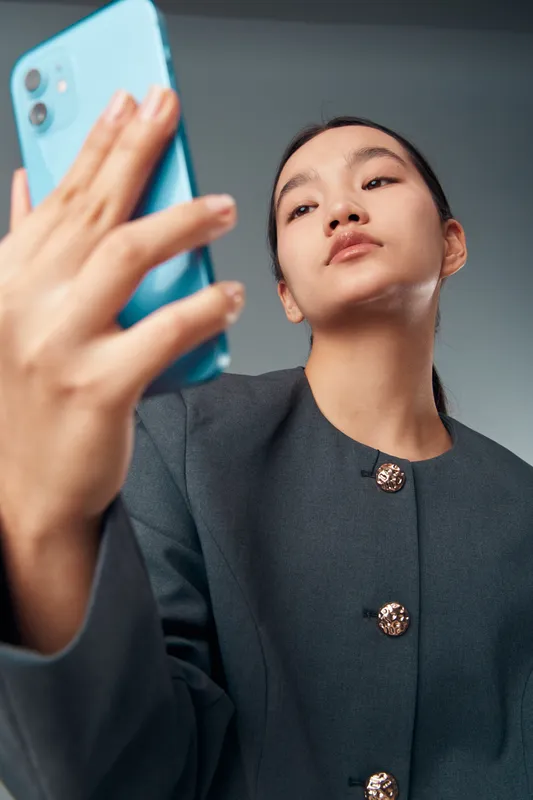 Young woman taking selfie with smartphone in hand indoors. Casual portrait, mobile phone, facial expression and digital device for social media, communication and technology usage.