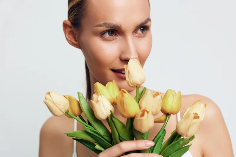 Woman portrait tulips flowers spring beauty skincare wellness closeup studio, female holding tulip bouquet near face, calm expression on white background, soft studio light, skincare care concept