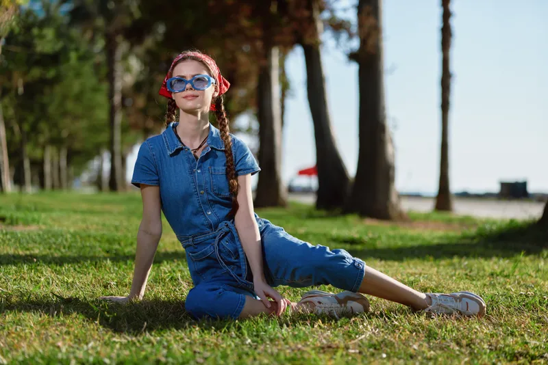 Lifestyle woman in modern boho-western denim street style with sunglasses relaxing outdoors on green grass, film color tone, casual summer fashion, young and stylish female