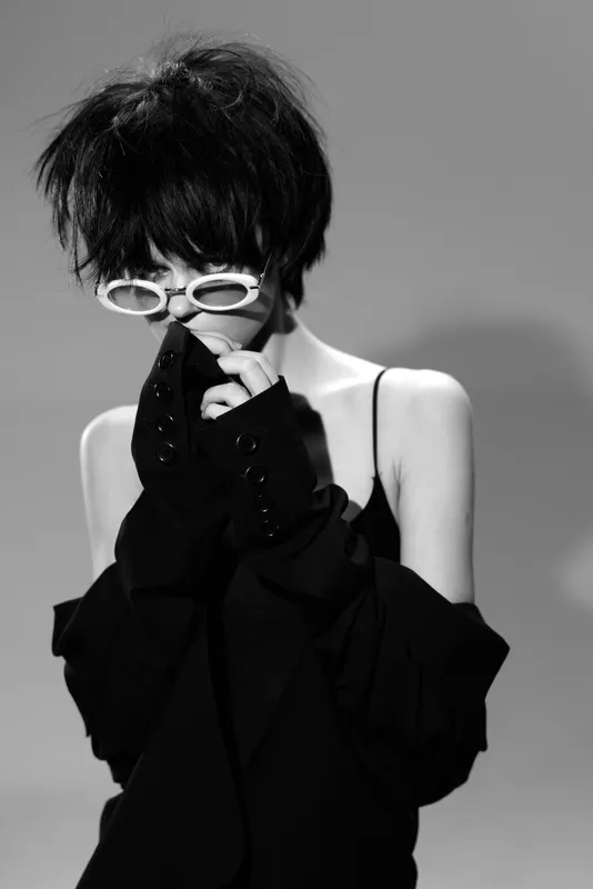 Stylish woman wearing white sunglasses and black clothing in a black and white portrait with a modern edgy look.