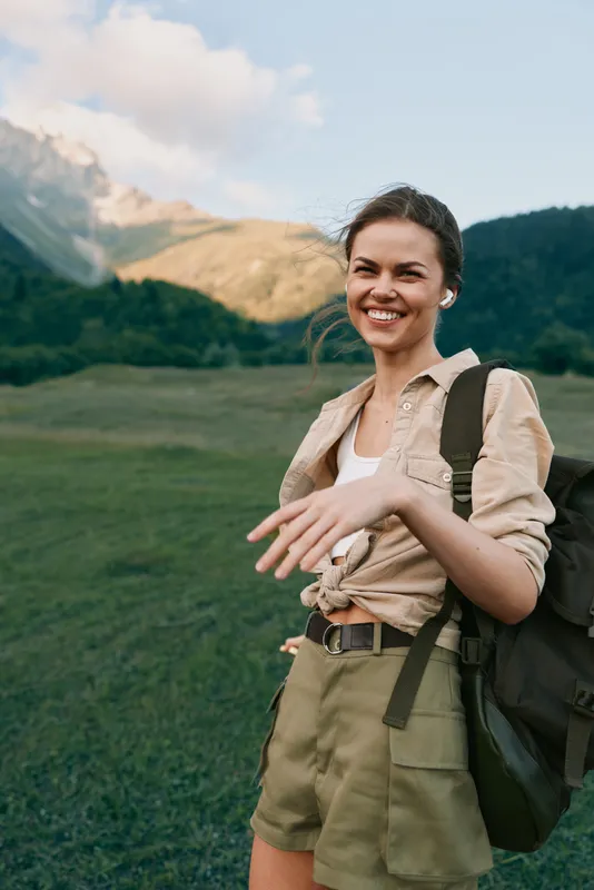 Young woman hikes through a sunlit mountain meadow with a backpack, smiling as she explores a rugged trail, embracing nature and adventure today, freedom.
