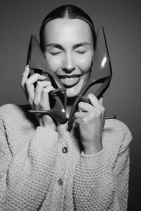 Happy Caucasian woman with light skin holding red high heels near face in studio. Concept of joy, fashion, and personal style.