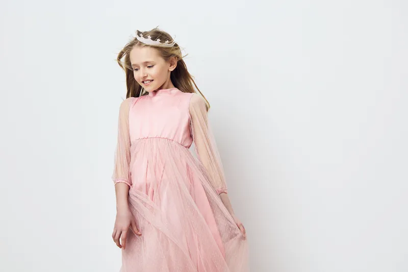 Cute girl in a pink tulle dress with a crown, smiling and looking down, perfect for children s fashion and portrait photography