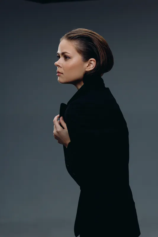 Profile of a serious woman in black jacket with slicked-back hair on gray background, stylish and modern concept