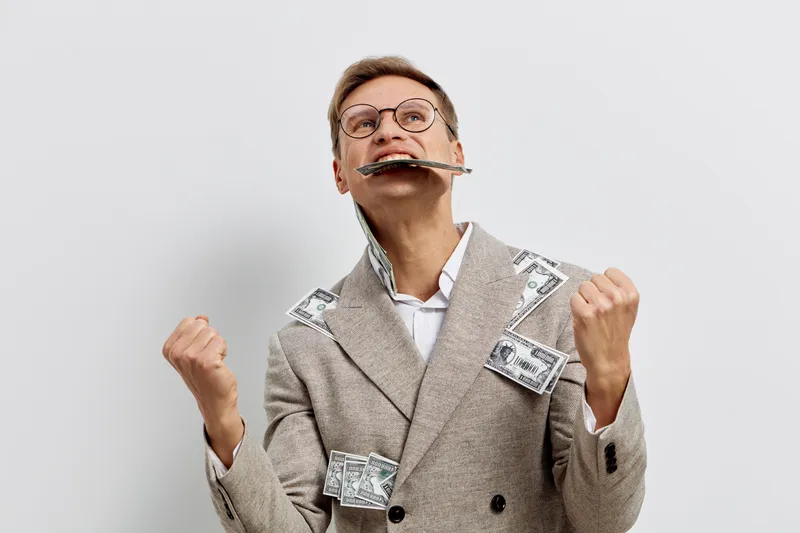 Smiling woman with glasses and short hair playfully holding a harmonica in her mouth, wearing a beige coat with dollar bill accessories, expressing joy, fun, and humor on plain white background. Peopl