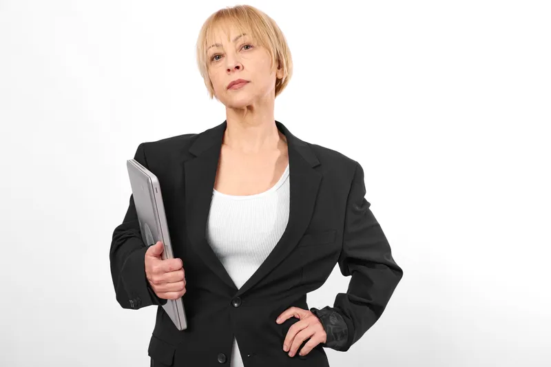 Older woman in business suit holding a notebook, confident studio portrait on white background, focused expression, corporate presentation concept, soft light