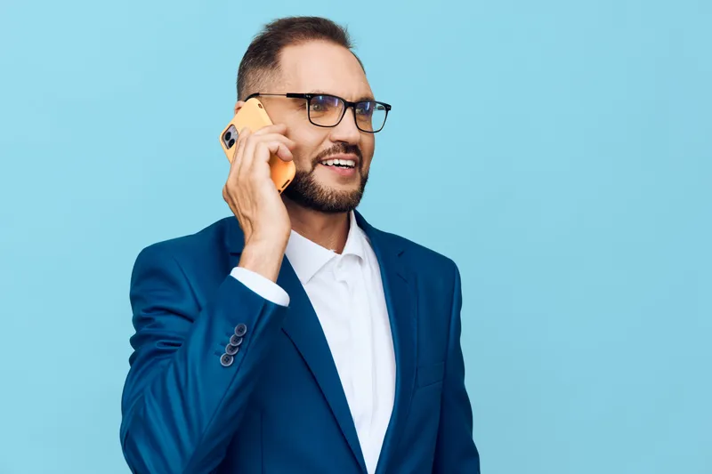 Businessman on a bright blue background, talking on a yellow phone. Confident, focused, and energetic, he projects professional calm and clear communication in a modern work setting.