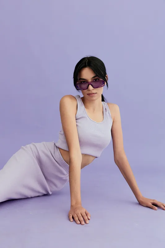 young woman wearing purple sunglasses and matching casual outfit poses on lavender background, showcasing summer fashion and confident style in soft pastel tones