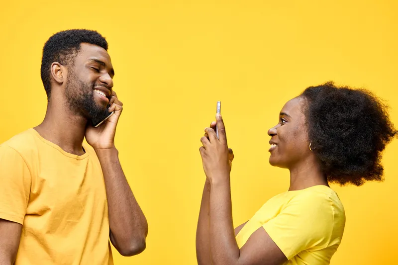 A joyful couple taking selfies with smartphones against a bright yellow background, showcasing happiness and connection, perfect for social media content