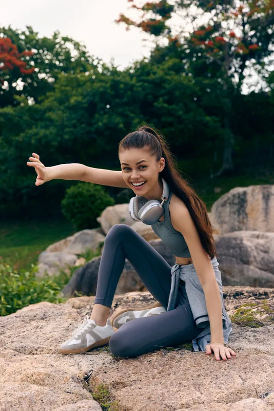 Active young woman enjoying outdoor workout in sporty attire, smiling and stretching on rocky terrain during a sunny day, showcasing a vibrant lifestyle