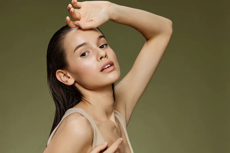 Young model with natural makeup posing gracefully against a soft green background, showcasing elegance and confidence in a minimalist setting