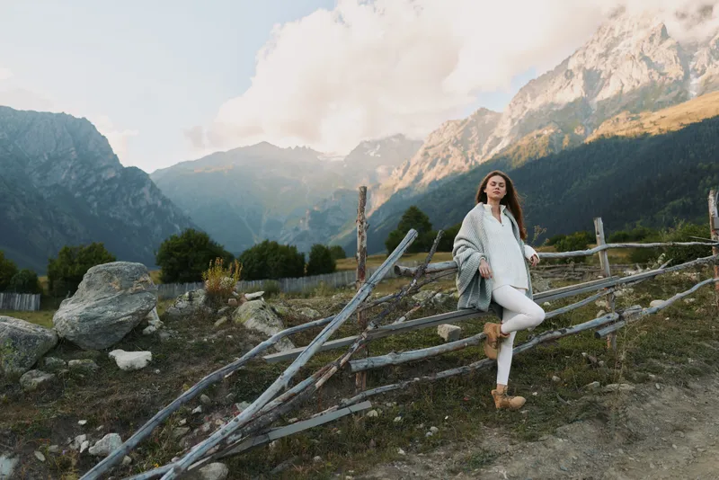 Cheerful woman outdoors, smiling in mountain landscape, casual chic pose, sunlit moment, natural colors, relaxed lifestyle, scenic backdrop with dramatic peaks,glow