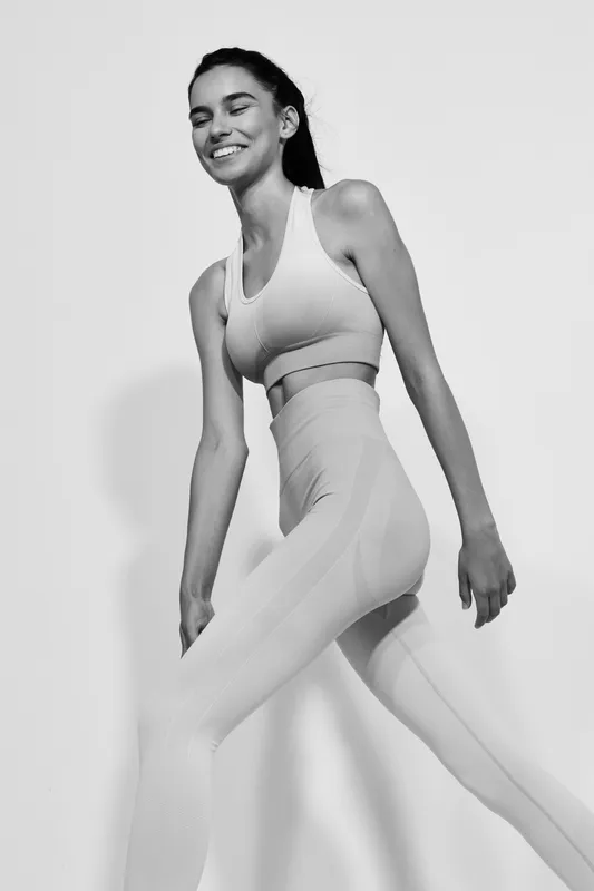 black and white woman sport fitness wearing seamless activewear smiling with eyes closed in dynamic pose on plain background, healthy lifestyle concept