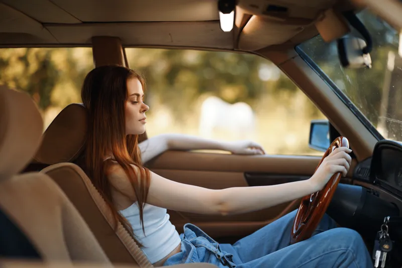 Young woman enjoying a serene drive in a vintage car, radiating calmness and confidence amidst a soft, warm background.