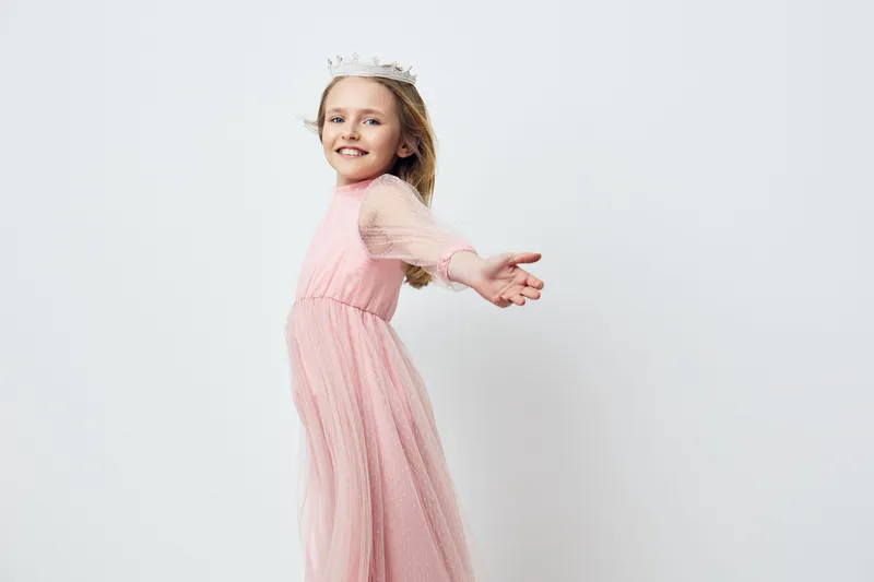 A joyful little girl in a pink dress twirls gracefully with outstretched arms, embodying happiness and innocence against a minimalist white background