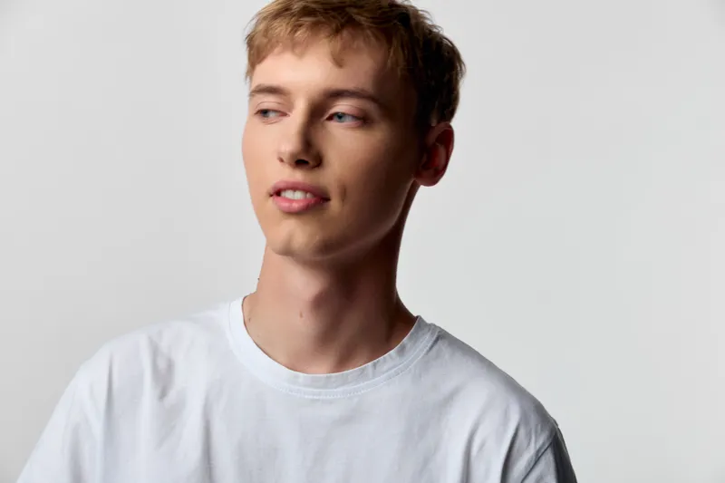 Young man wearing a white tshirt in studio looking away with a casual expression, clean background, minimal fashion shot for lifestyle and advertising use